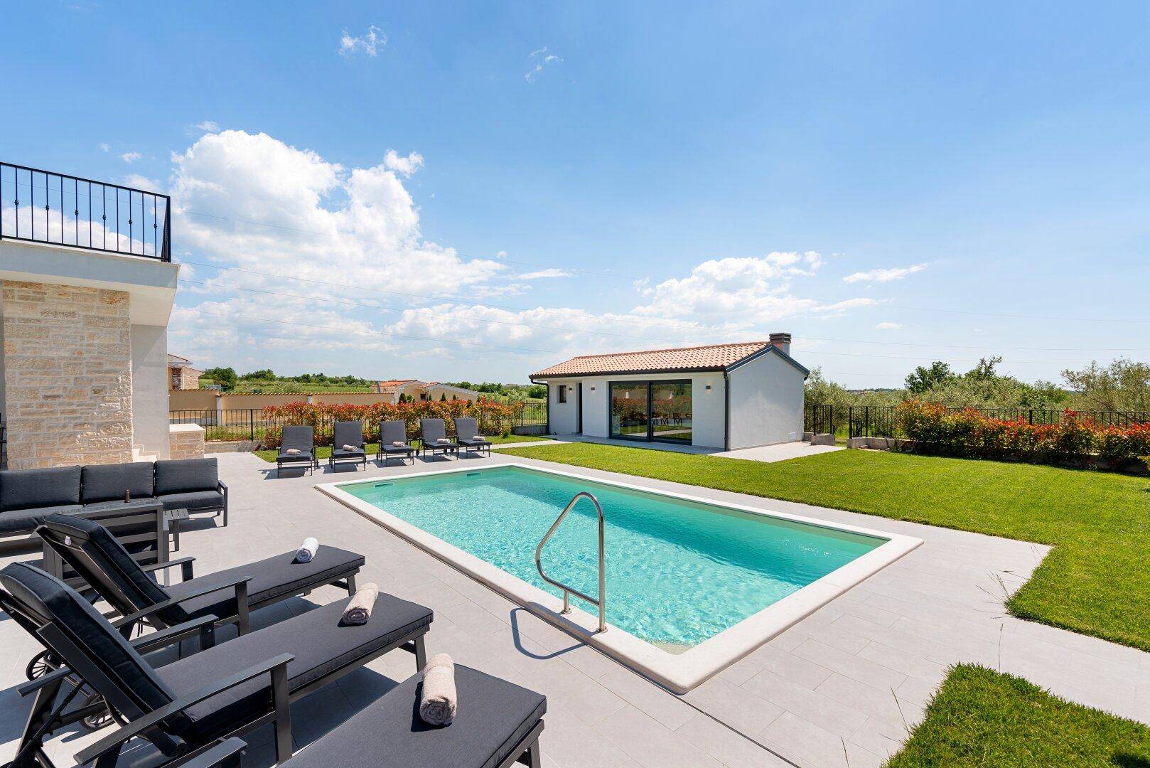 Sonniger Außenbereich mit Pool, Liegestühlen und Lounge-Möbeln vor der modernen Villa.