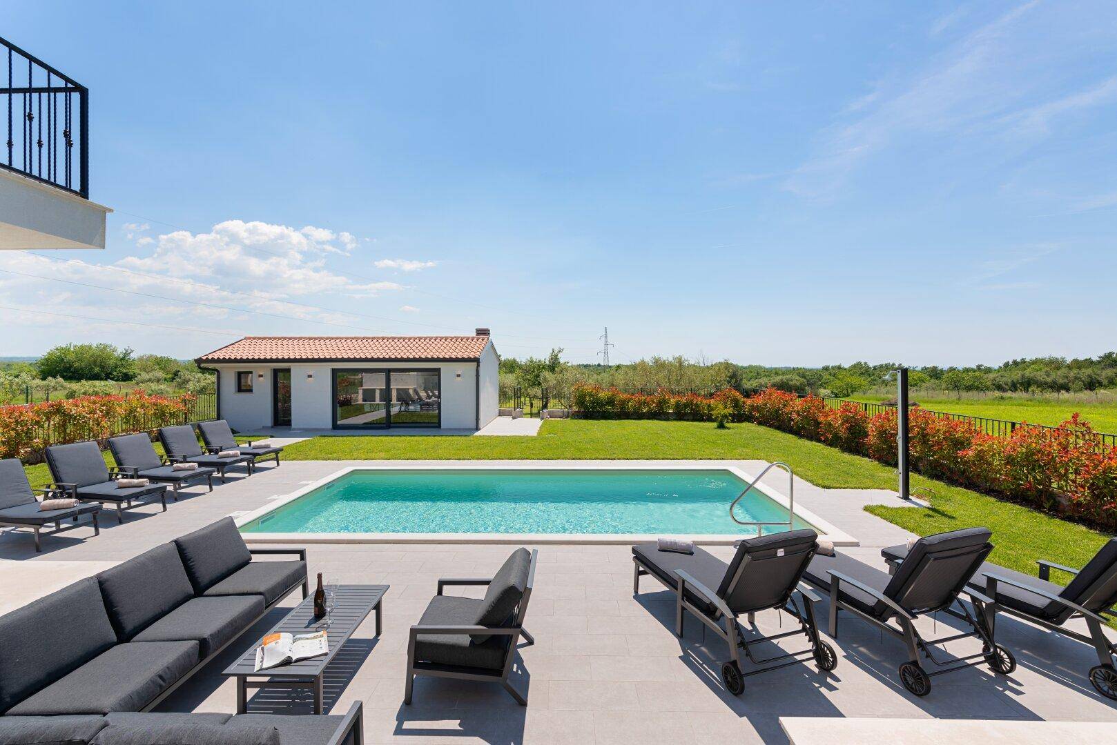 Sonniger Poolbereich mit Liegestühlen und Blick auf das Nebengebäude und die grüne Landschaft.