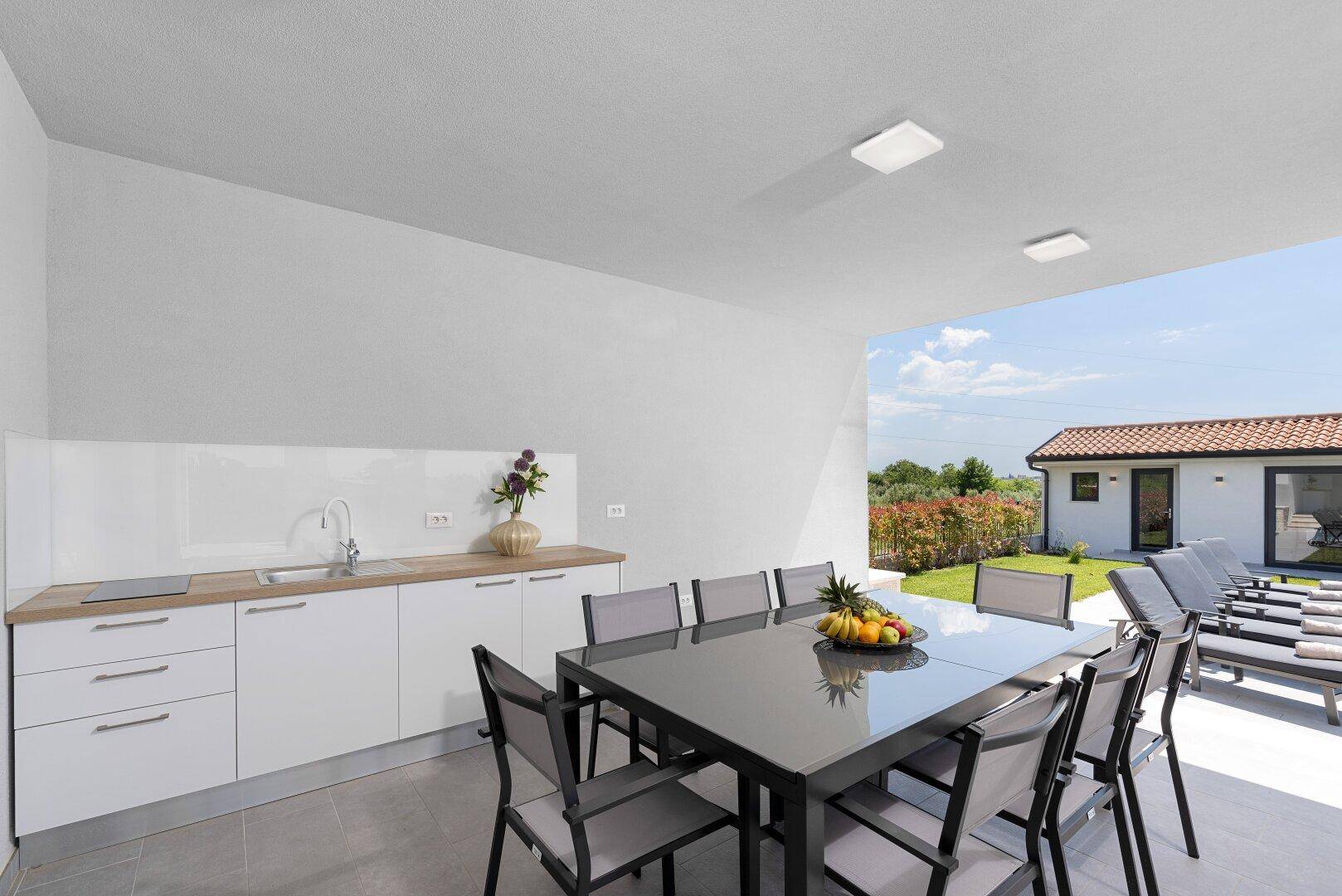 Überdachte Terrasse mit Esstisch und integrierter Außenküche, ideal für Mahlzeiten im Freien.