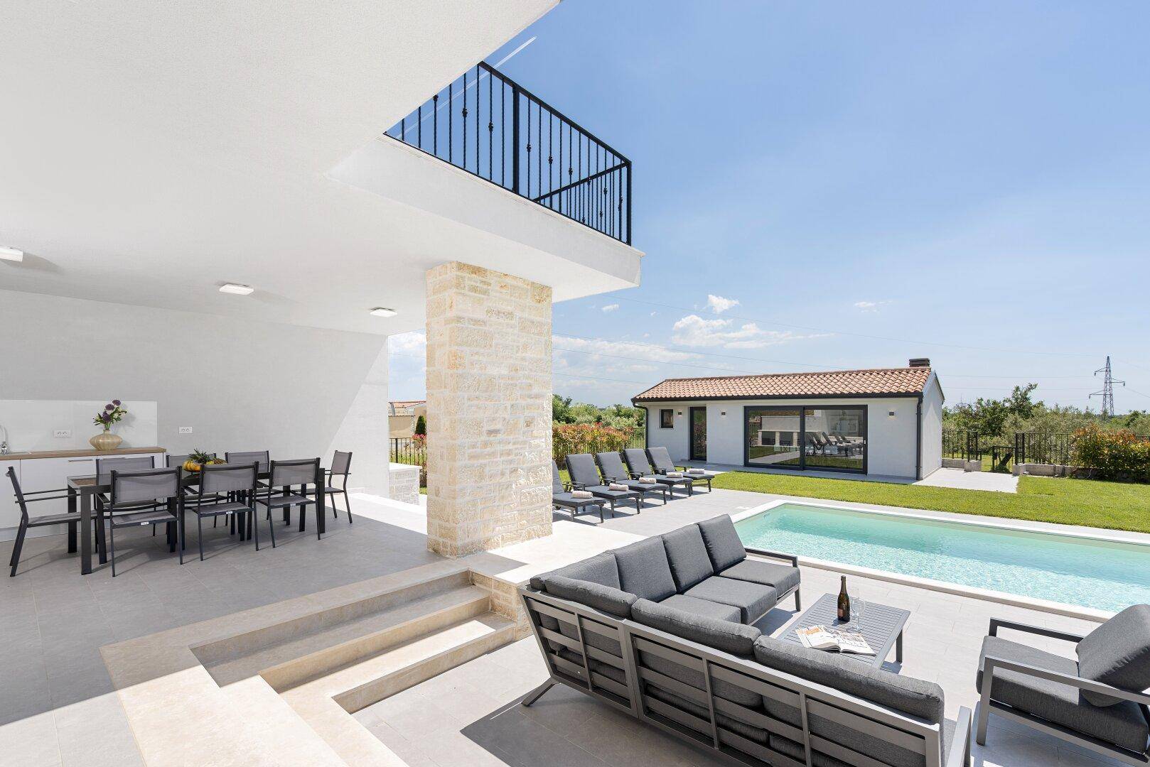 Großzügige Terrasse mit Lounge-Möbeln und Essbereich, mit Blick auf den Pool und die grüne Umgebung.