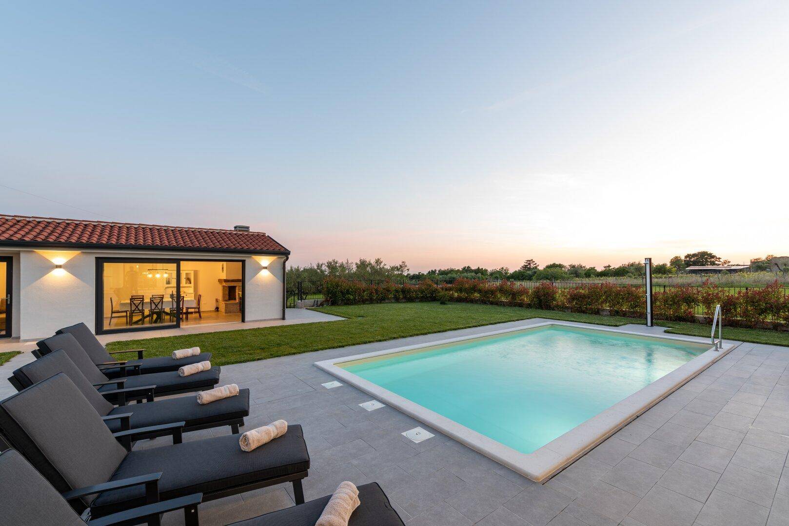 Abendliche Szene mit Liegestühlen am Pool und dem beleuchteten Nebengebäude im Hintergrund.