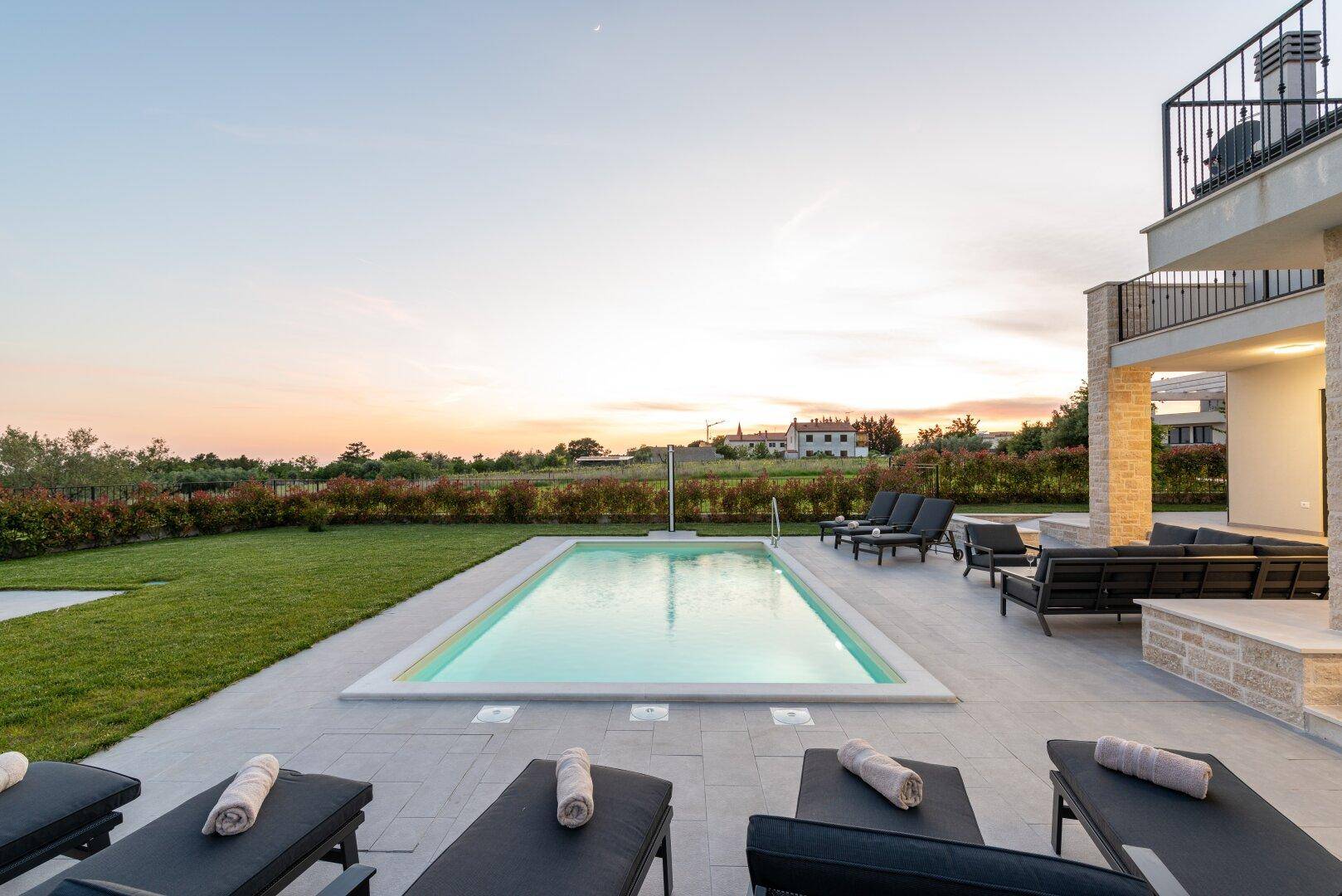 Weitläufiger Poolbereich mit Liegestühlen und Lounge-Möbeln bei Sonnenuntergang.