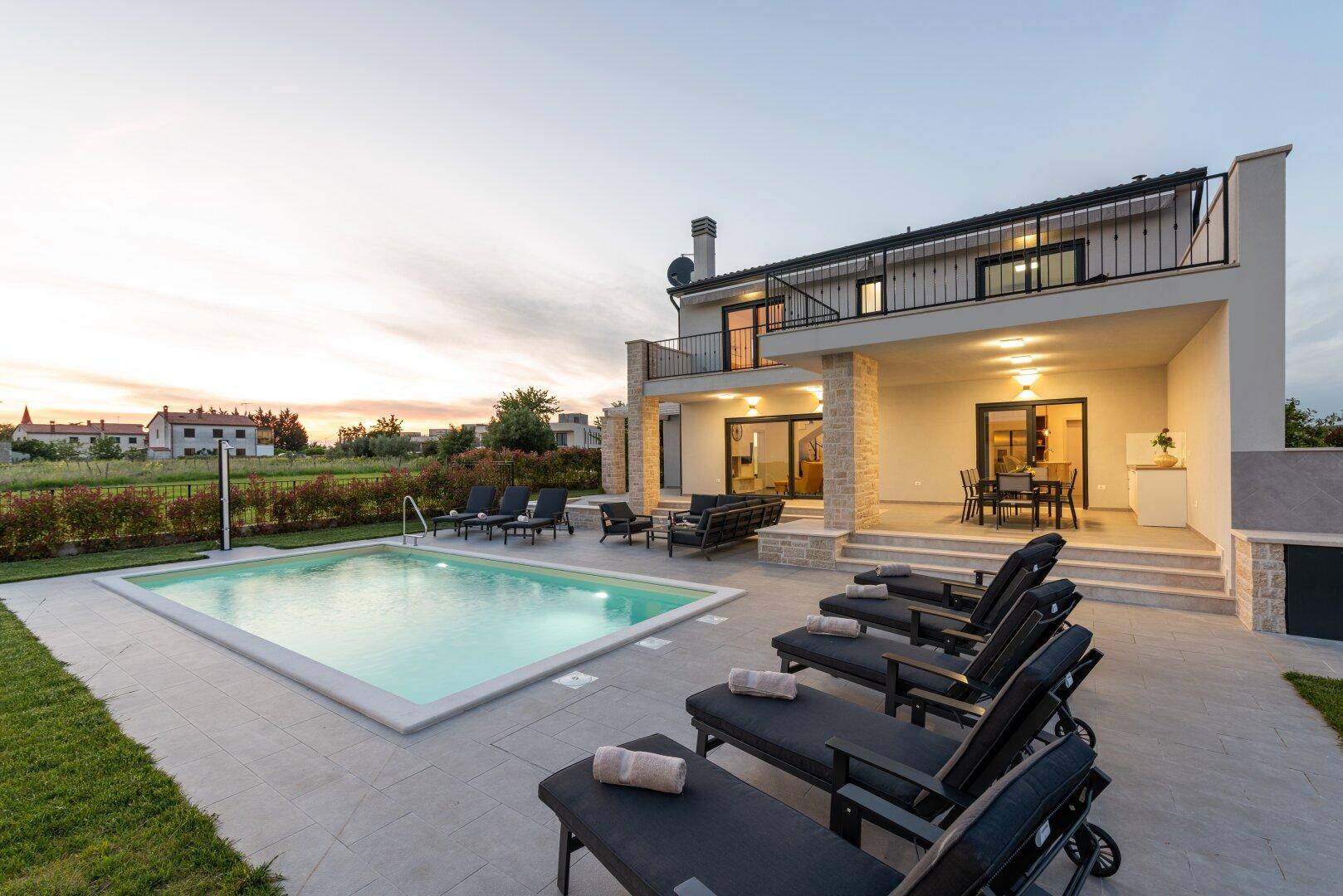 Abendliche Stimmung auf der Poolterrasse mit beleuchtetem Pool und bequemen Liegestühlen.