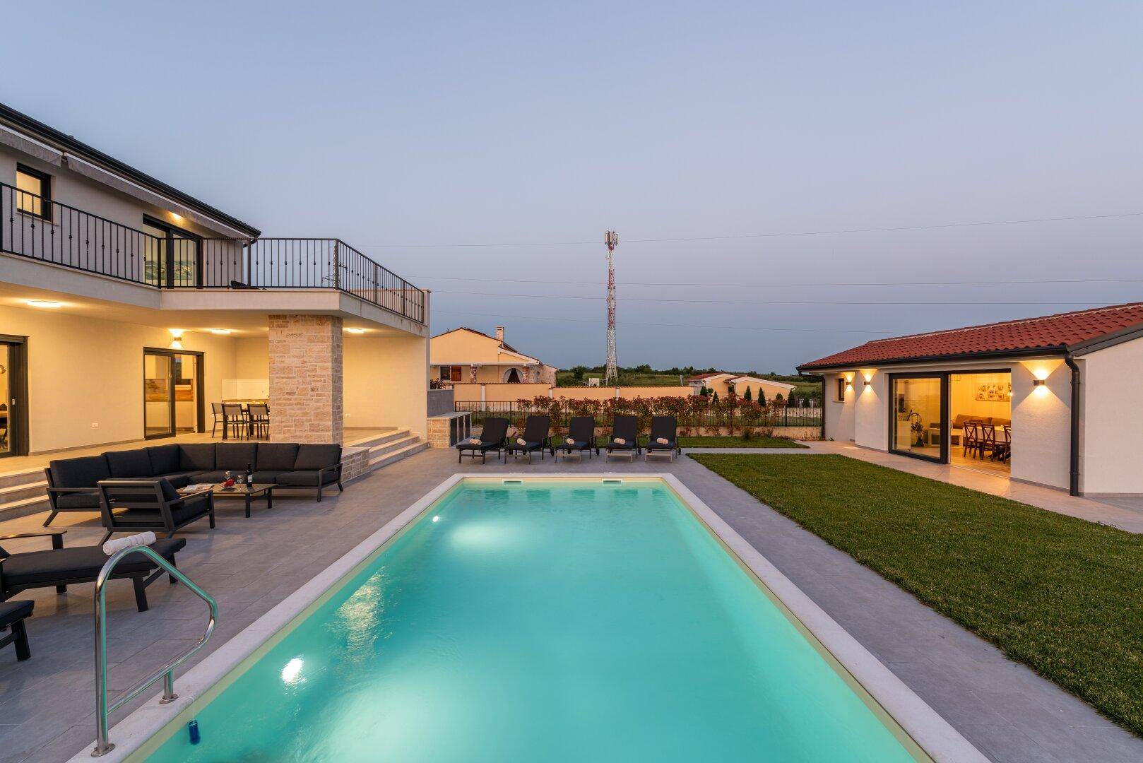 Abendliche Ansicht des Pools mit Liegestühlen und beleuchtetem Nebengebäude in der Ferne.