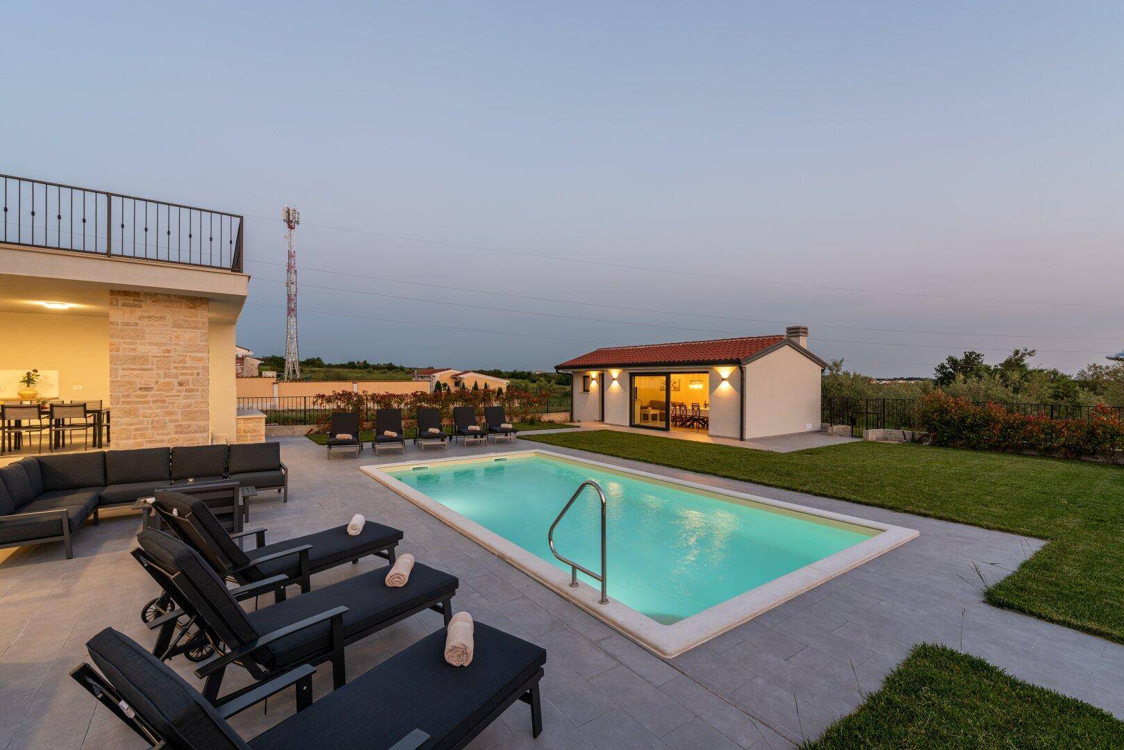 Abendlicher Panoramablick auf den beleuchteten Pool, Lounge-Bereich und das Nebengebäude.