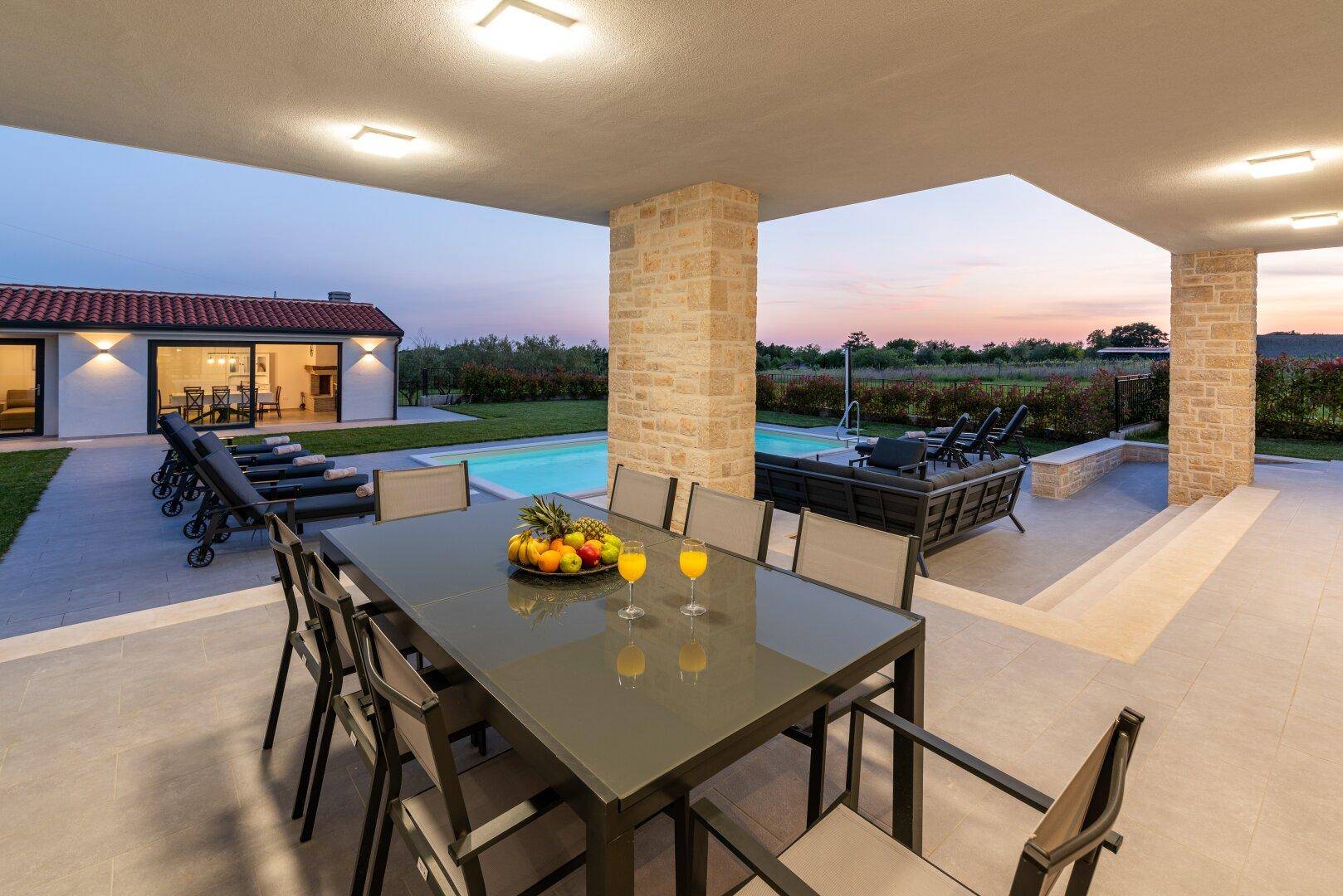 Abendlicher Essbereich im Freien auf der überdachten Terrasse mit Blick auf den beleuchteten Pool.