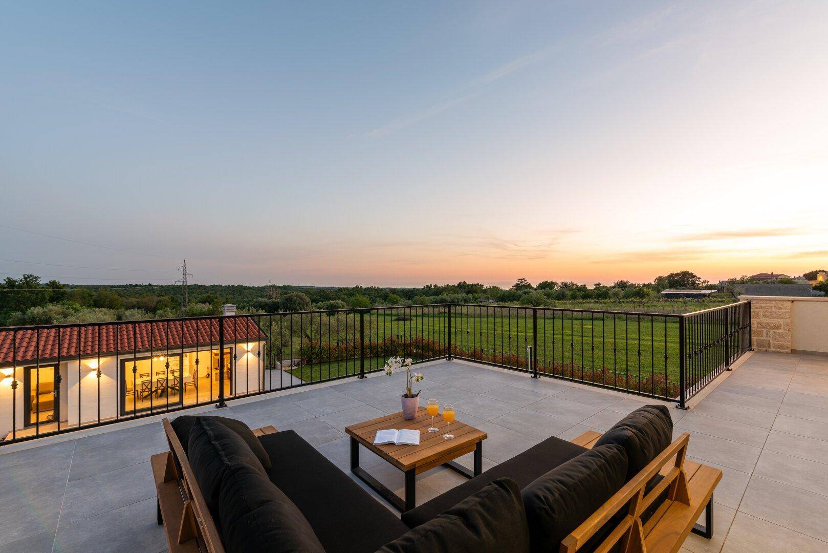 Gemütliche Dachterrasse mit Lounge-Möbeln und weitem Blick über die Landschaft bei Sonnenuntergang.