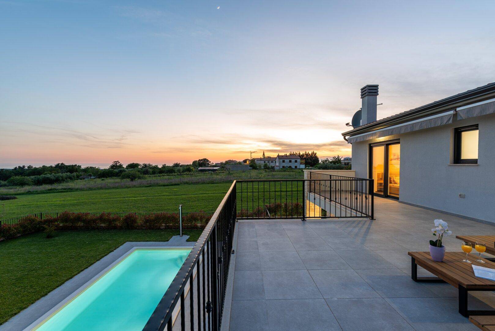Terrasse des Hauses bei Sonnenuntergang mit Blick auf den beleuchteten Pool und die weite Landschaft.