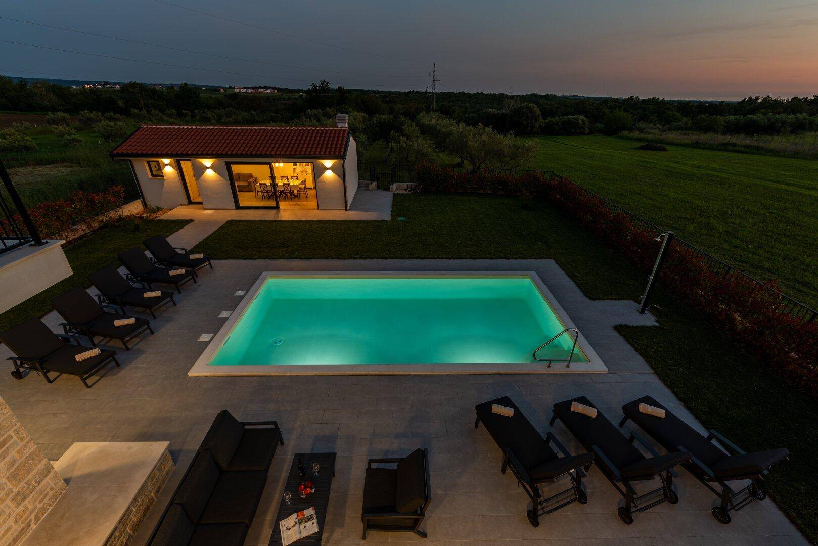 Abendliche Vogelperspektive der gesamten Anlage mit beleuchtetem Pool und weitläufigem Garten.