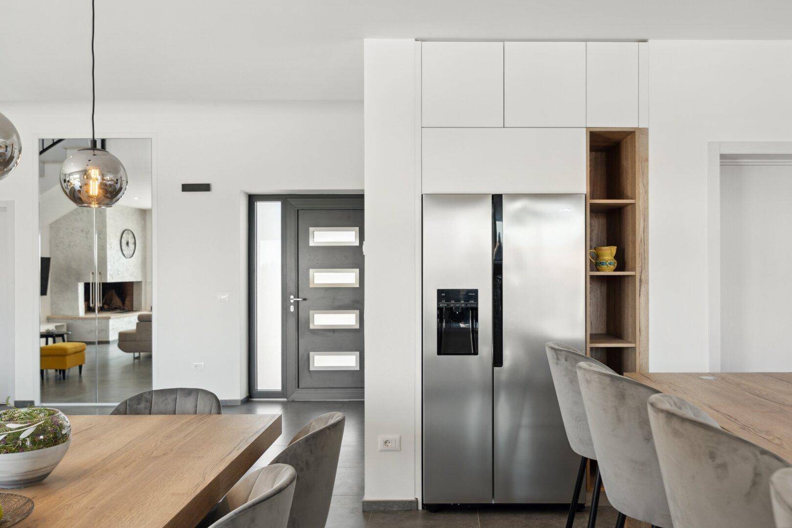 Eingangsbereich mit großem Kühlschrank und Spiegel, der den offenen Wohnbereich reflektiert.
