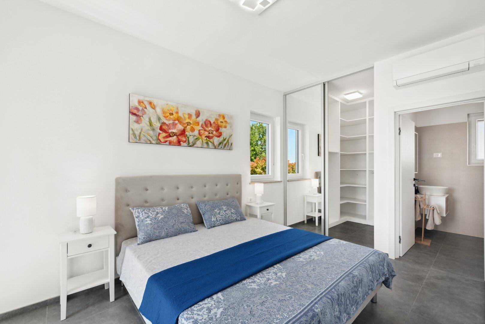 Helles Schlafzimmer mit Doppelbett, Einbauschrank und direktem Zugang zum modernen Badezimmer.