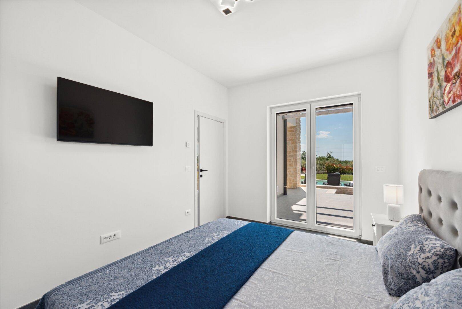 Komfortables Schlafzimmer mit Wandfernseher und großen Schiebetüren zum Außenbereich mit Pool.
