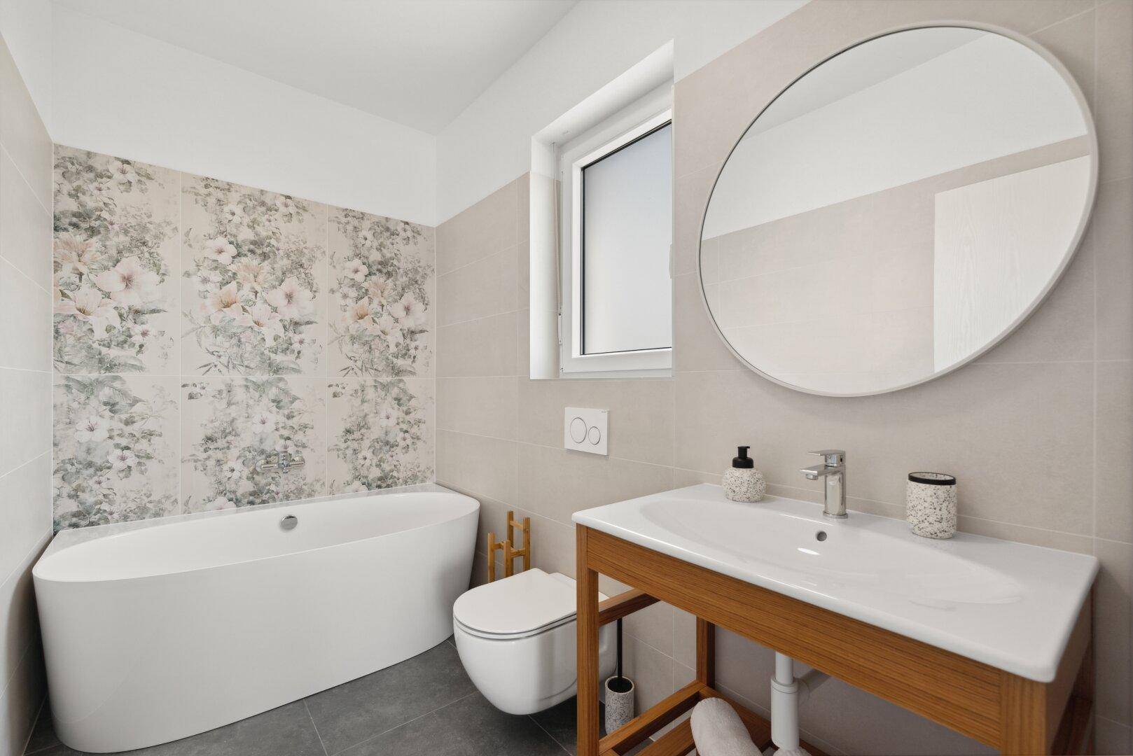 Elegantes Badezimmer mit freistehender Badewanne, Fenster und floraler Wandgestaltung über der Wanne.