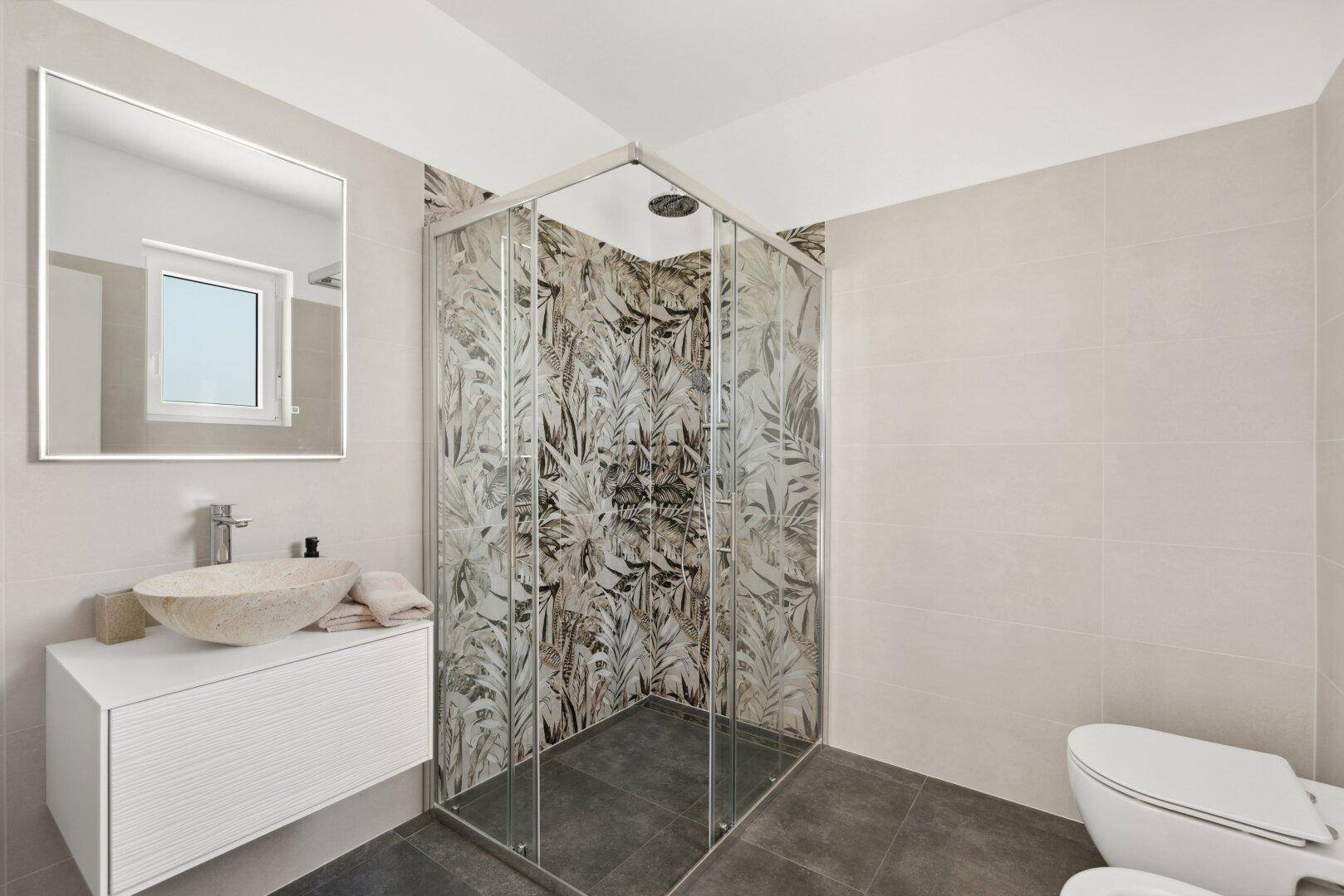 Modernes Badezimmer mit Eckdusche, Steinwaschbecken und floral gemusterten Duschfliesen.