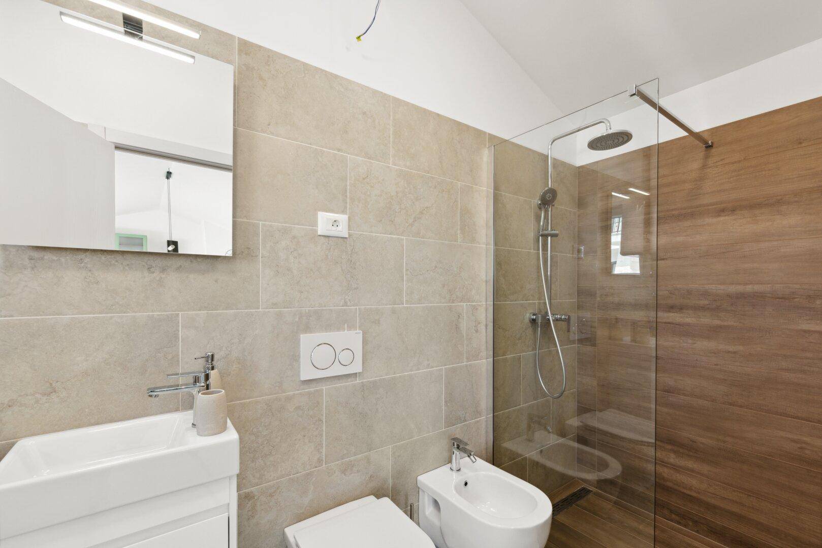 Modernes Badezimmer mit beigefarbenen Fliesen, begehbarer Dusche, Bidet und Einzelwaschbecken.