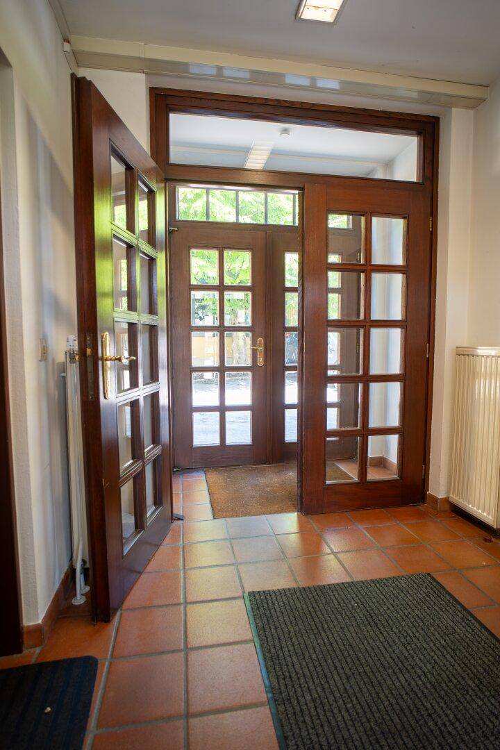 Heller Eingangsbereich mit großen Glastüren, Fliesenboden und viel natürlichem Licht.