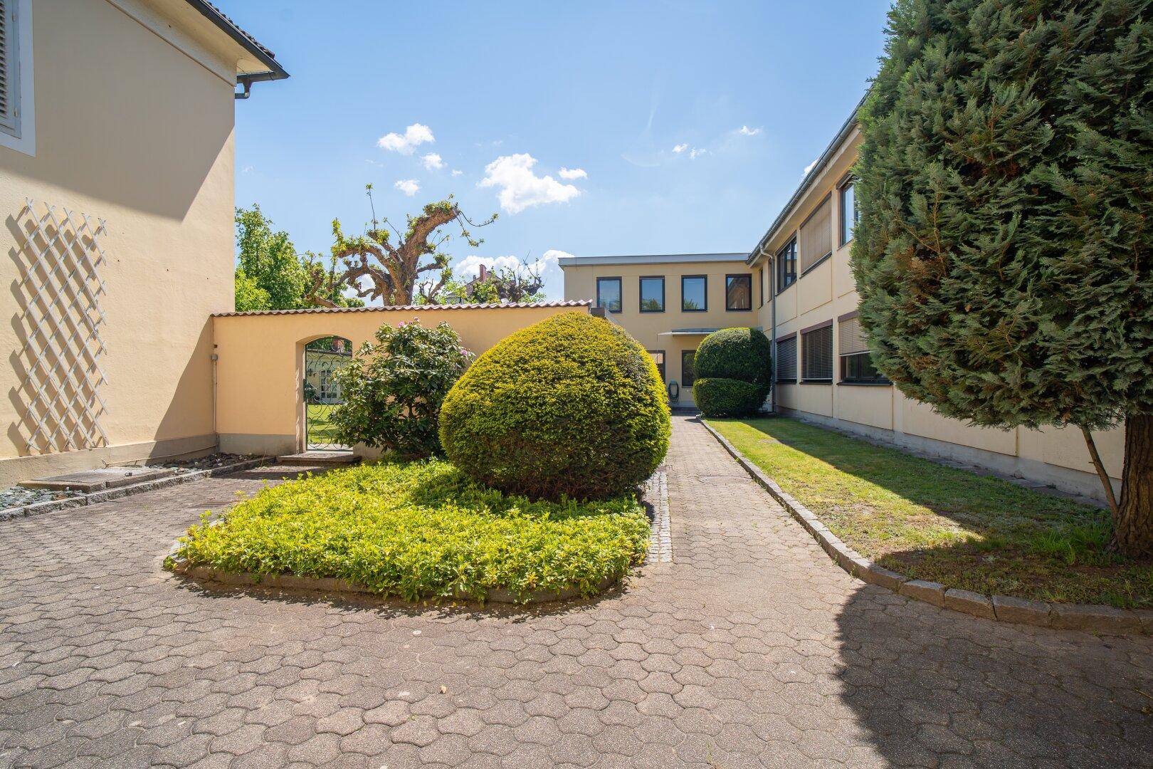 Gepflasterter Innenhof mit gepflegten Grünflächen, Sträuchern und einem sonnigen Ambiente.