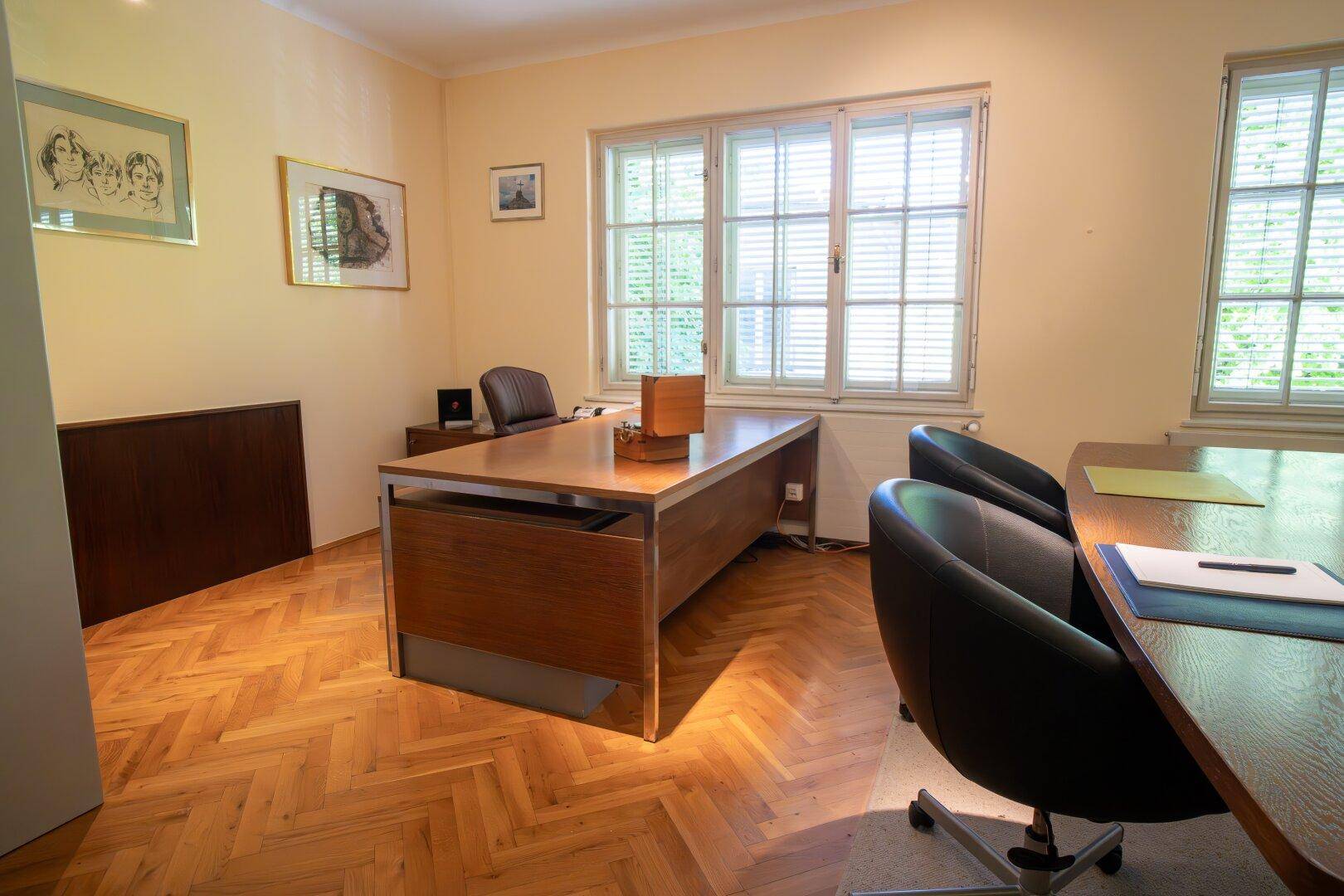 Büro mit klassischem Fischgrätparkett, großen Fenstern und einem Konferenztisch für Besprechungen.