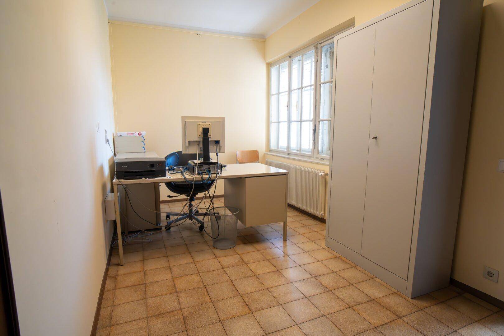 Kleineres Büro mit Fliesenboden, einem Arbeitsplatz und einem großen Schrank für Stauraum.