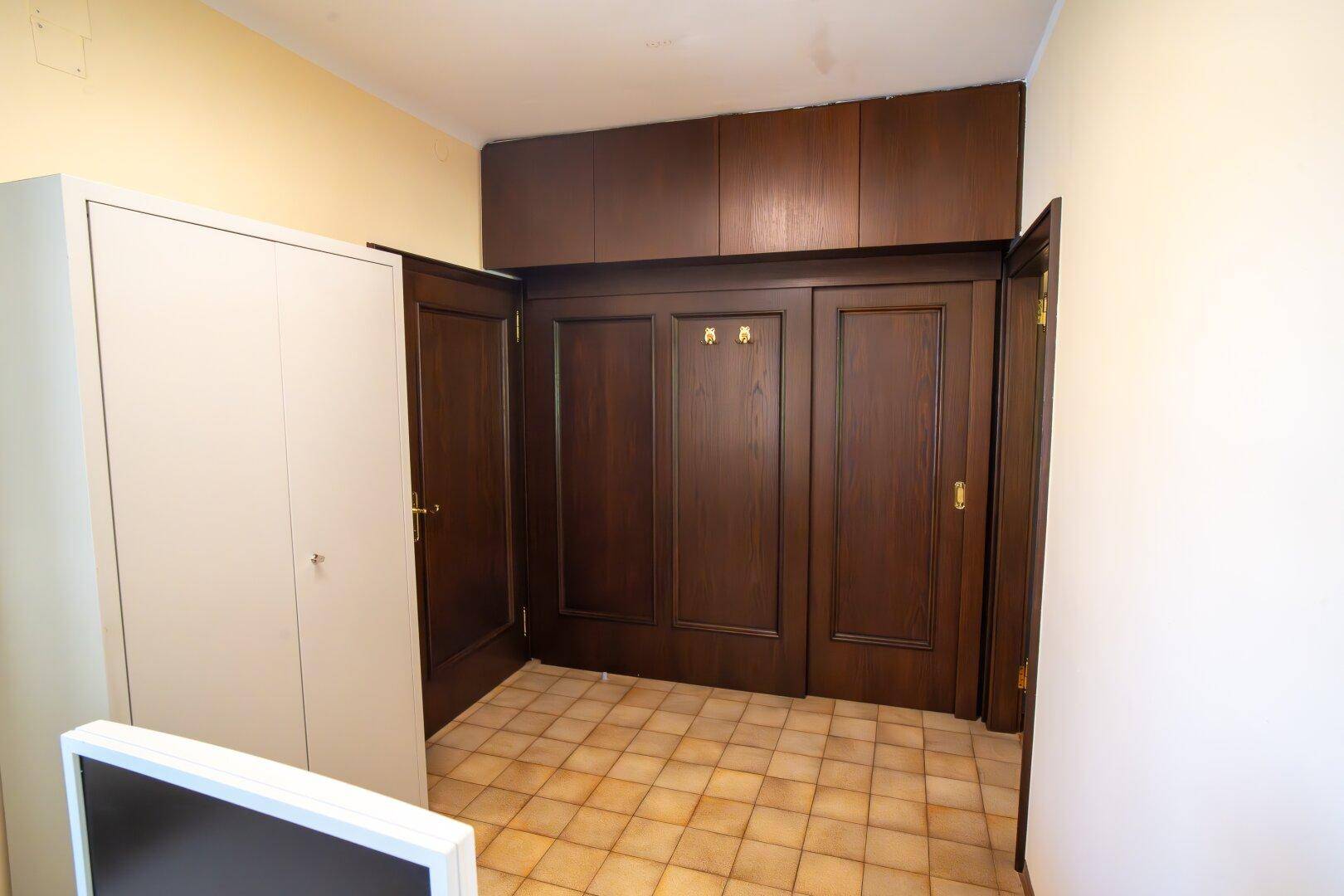 Eingangsbereich mit dunklen Holztüren, Einbauschränken und einem praktischen Fliesenboden.