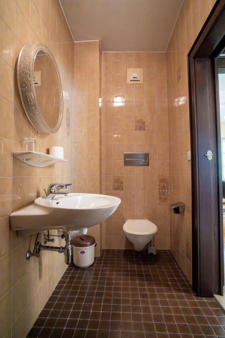 Gefliestes Badezimmer mit Wand-WC, Waschbecken und einem runden Spiegel in warmen Beigetönen.