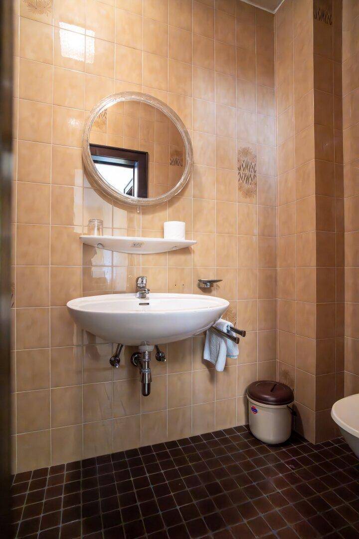 Badezimmer mit beigefarbenen Wandfliesen, einem Waschbecken und einem runden Spiegel.