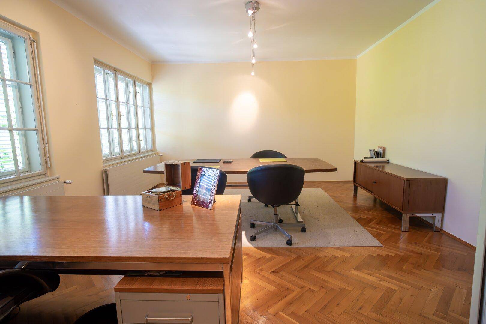Helles Büro mit Holzschreibtischen, ergonomischen Stühlen und natürlichem Lichteinfall durch mehrere Fenster.