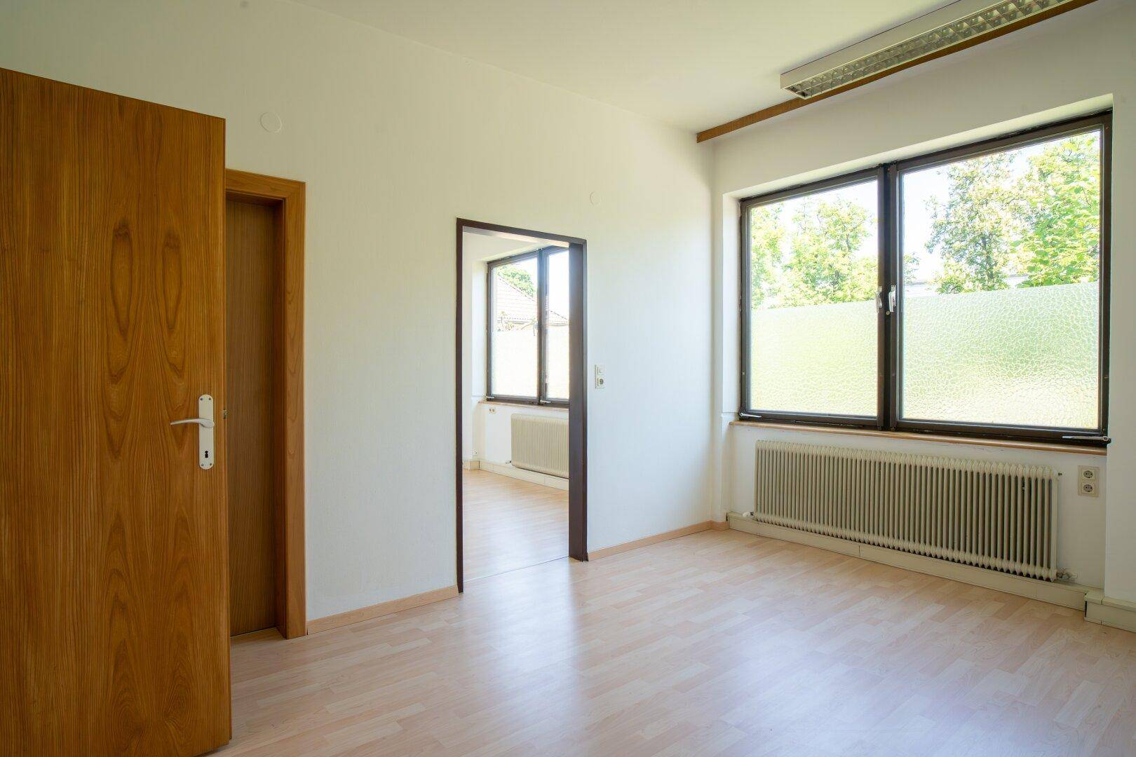 Leeres Büro mit Laminatboden, weißen Wänden und Holztüren, das viel Tageslicht erhält.