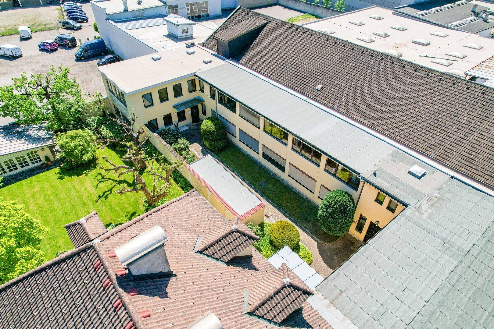 Weitläufige Luftaufnahme eines Gebäudekomplexes mit verschiedenen Dächern und Grünflächen.