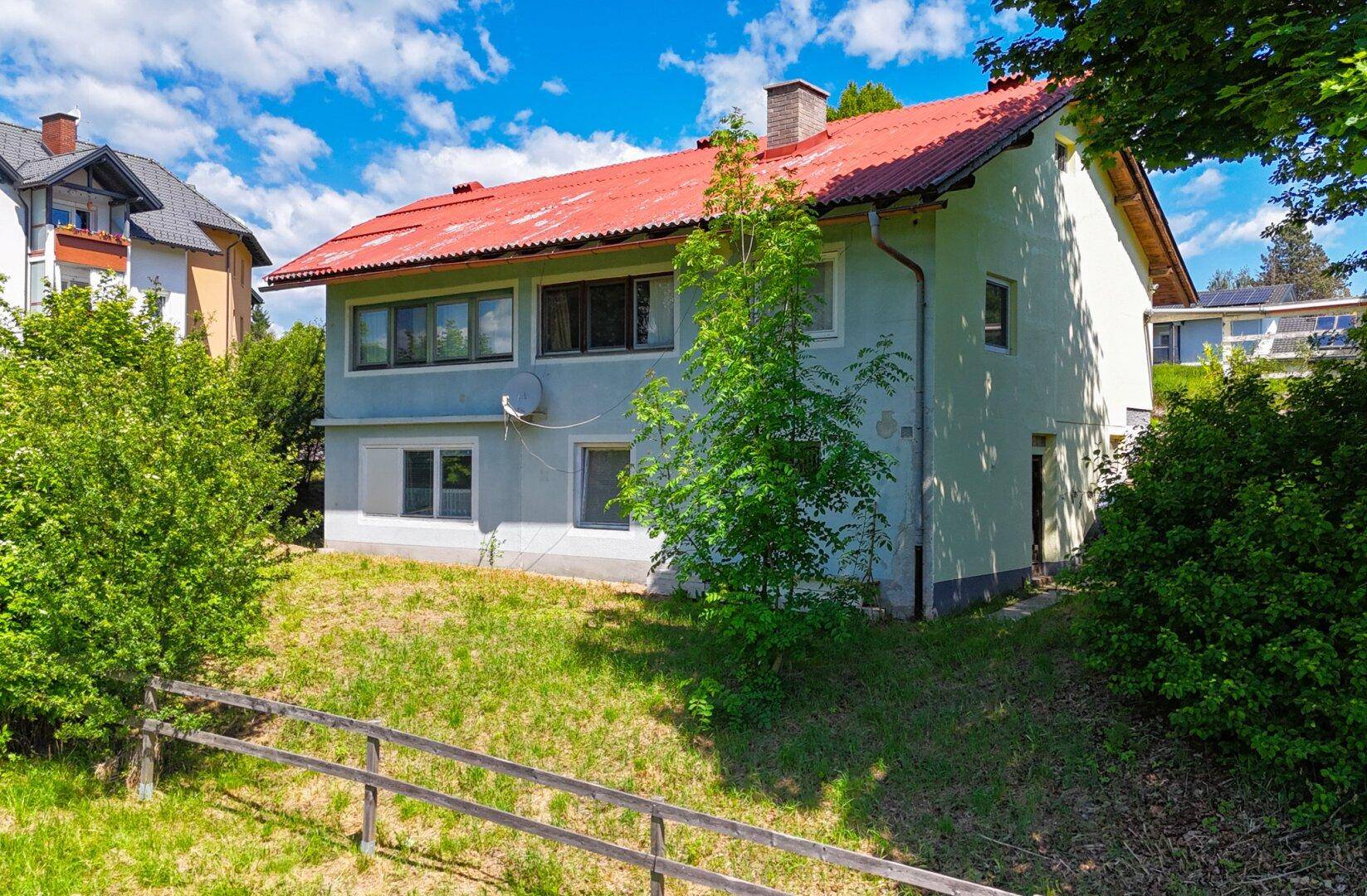 Ansicht des Wohnhauses mit rotem Dach und grüner Umgebung an einem sonnigen Tag.