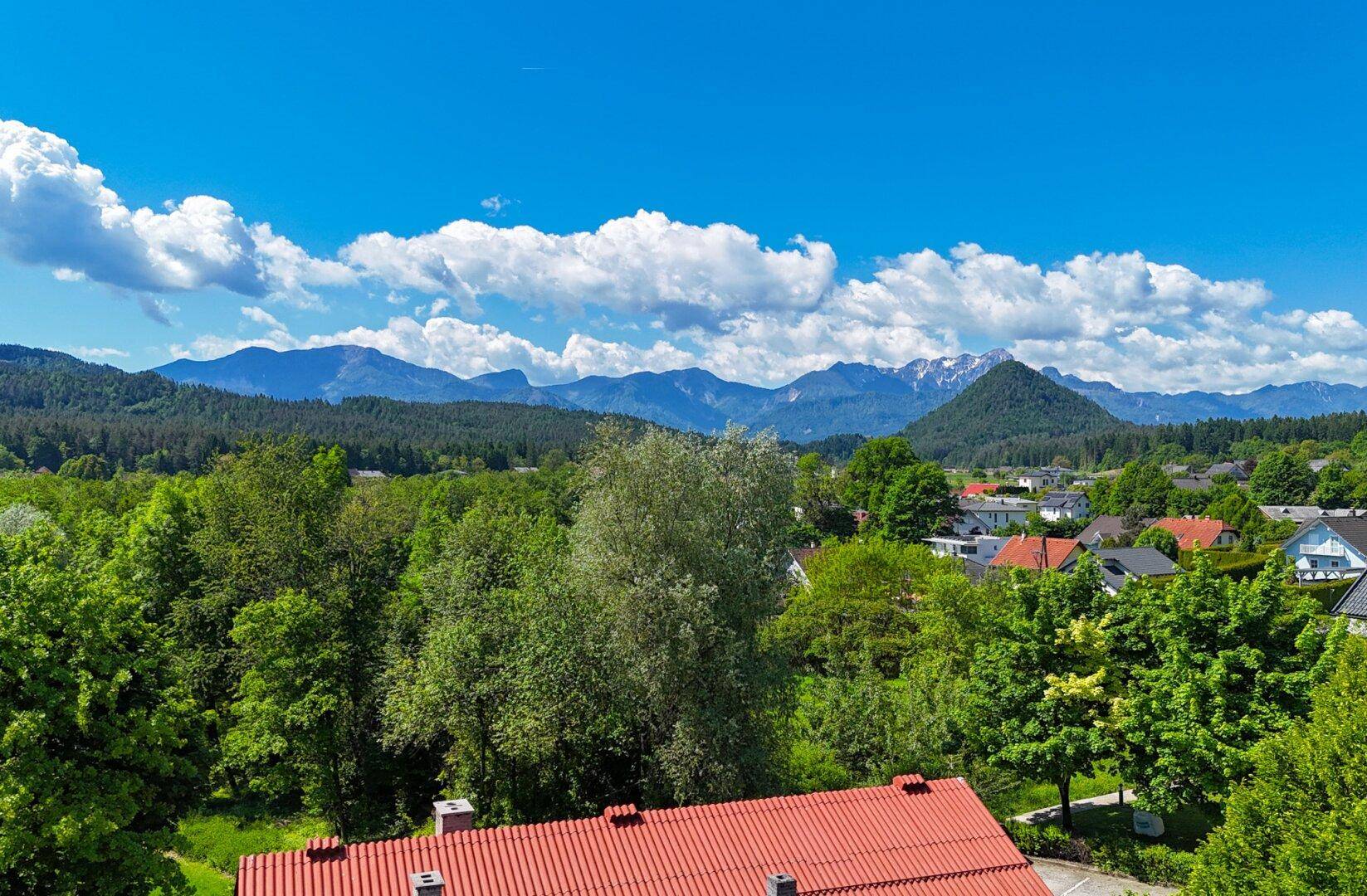 Weitläufiger Blick über die grüne Landschaft mit Häusern und majestätischen Bergen am Horizont.
