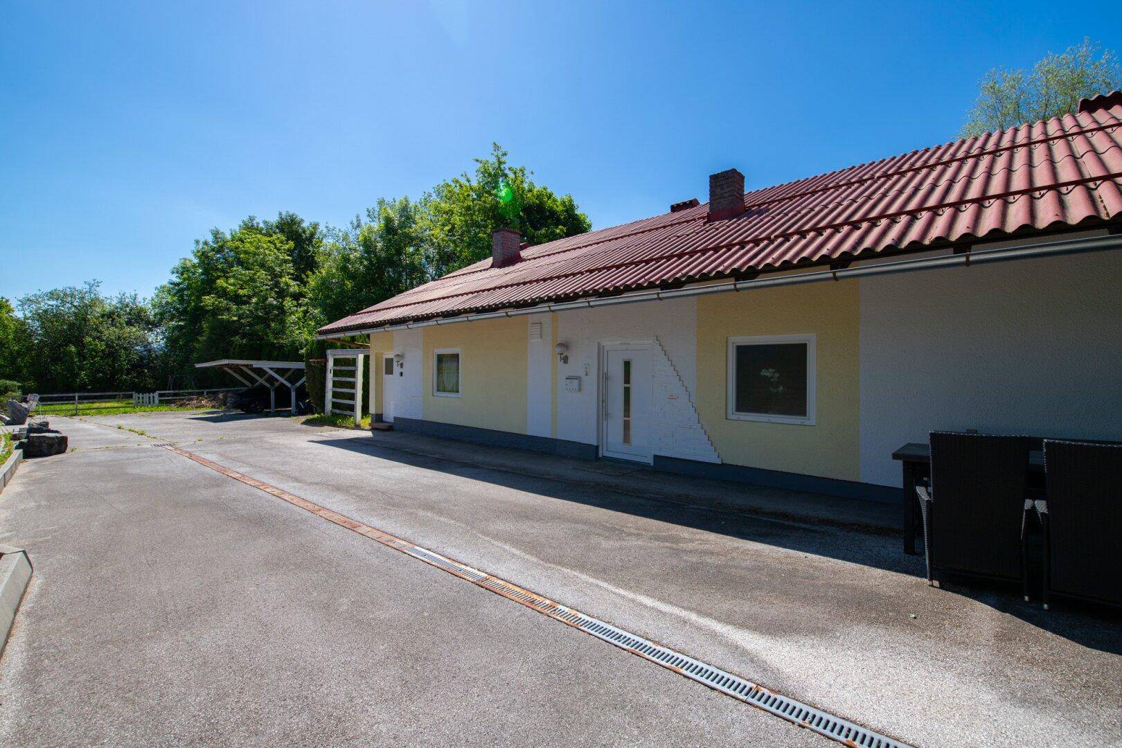 Zufahrt zum Haus mit gelber Fassade und rotem Dach, umgeben von Bäumen.