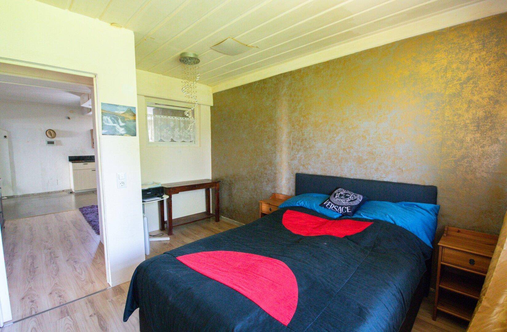 Schlafzimmer mit Doppelbett, Laminatboden und gold-gemusterter Akzentwand.