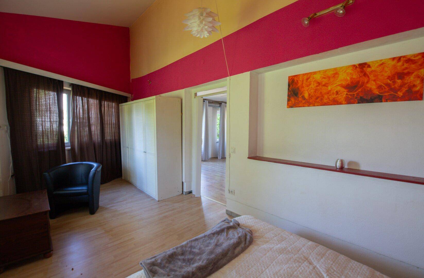 Helles Schlafzimmer mit Laminatboden, weißem Kleiderschrank und pinker Wandgestaltung.