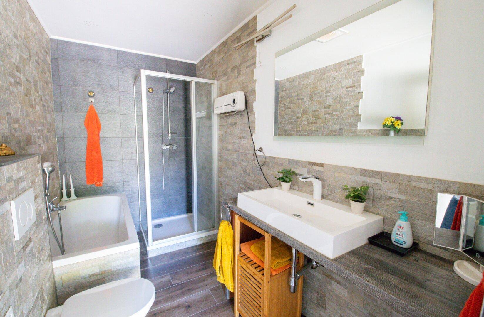 Modernes Badezimmer mit Dusche, Badewanne, Einzelwaschbecken und grauen Fliesen.