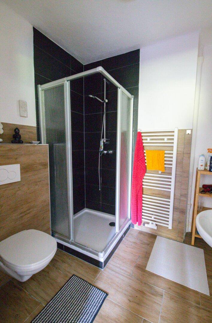 Badezimmer mit Duschkabine, Wand-WC und Holzoptik-Fliesen.