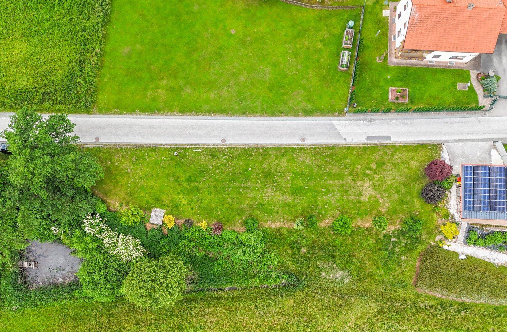 Luftaufnahme eines Grundstücks mit Straße, grünen Flächen, einem Haus und einem kleinen Teich.