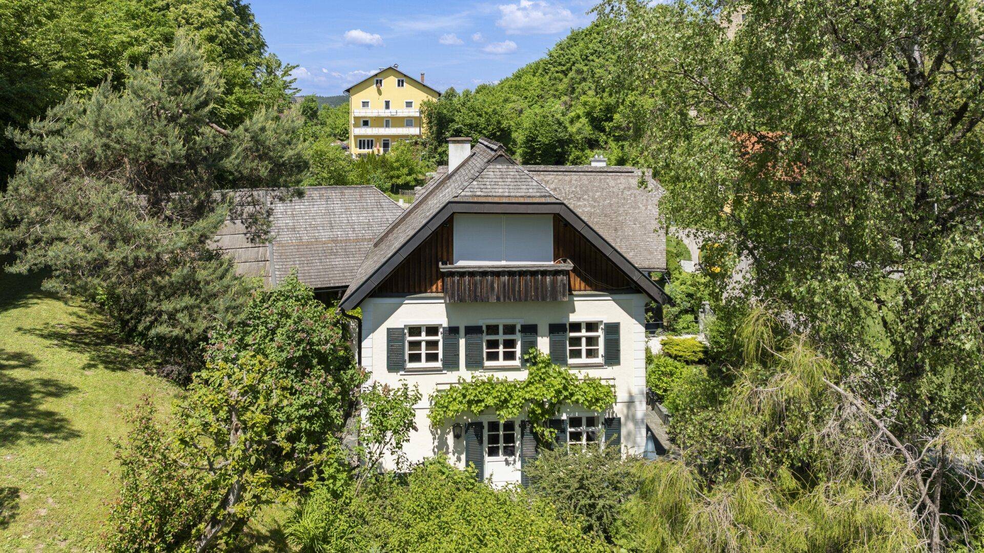 Charmantes Landhaus mit traditioneller Architektur, umgeben von üppigem Grün und Bäumen.