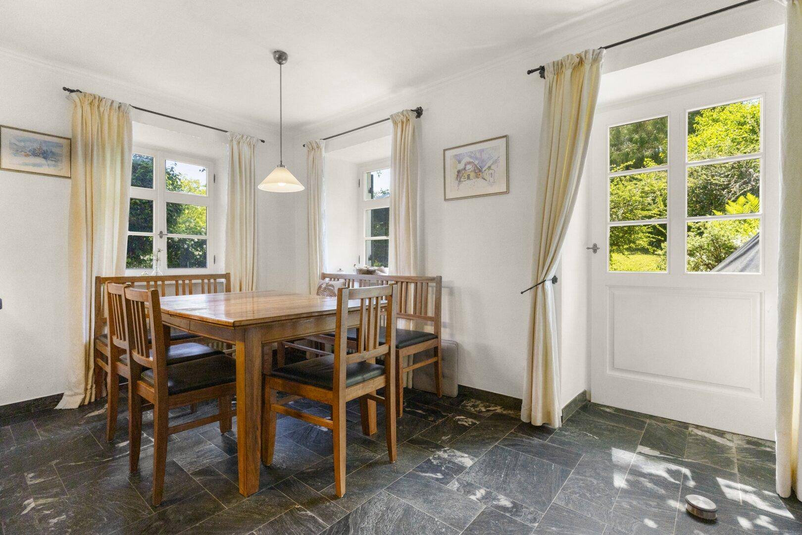 Gemütlicher Essbereich mit Holztisch, Steinboden und direktem Zugang zum Garten.