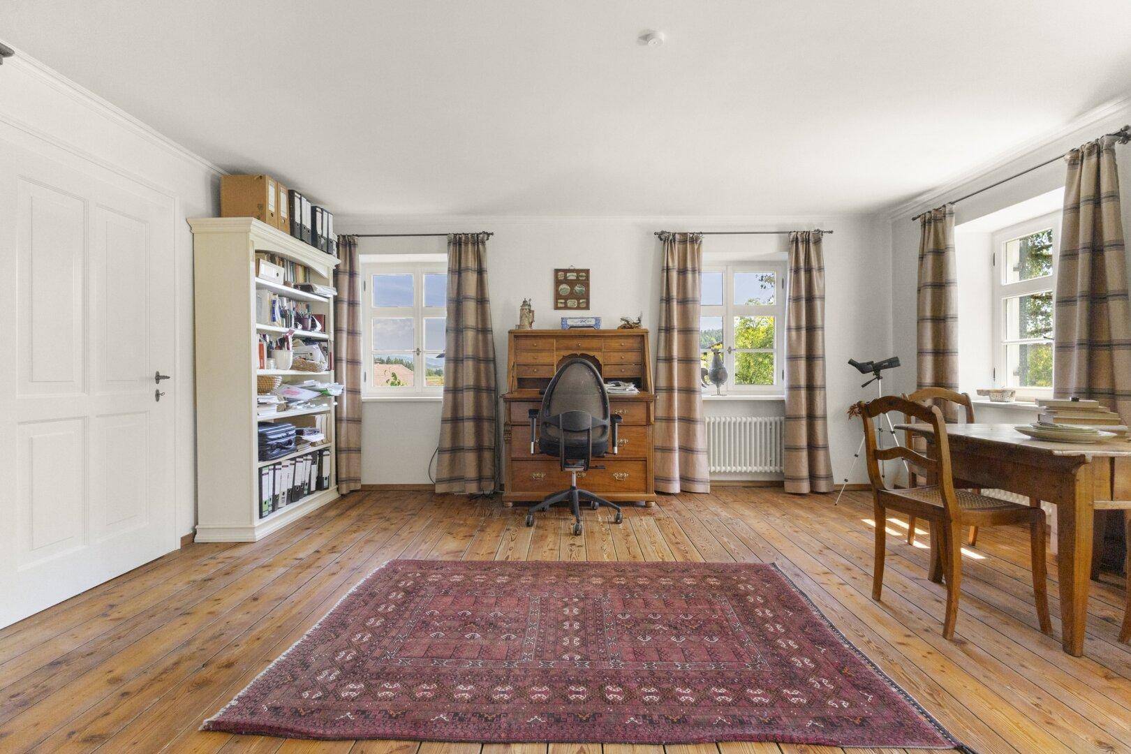 Geräumiges Arbeitszimmer mit breiten Holzdielen, einem Schreibtisch und Blick ins Grüne.