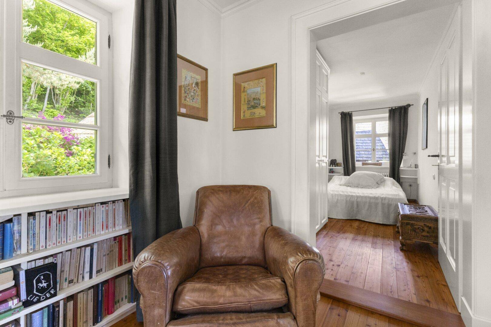 Gemütliche Leseecke mit Ledersessel und Bücherregal, angrenzend an ein Schlafzimmer.