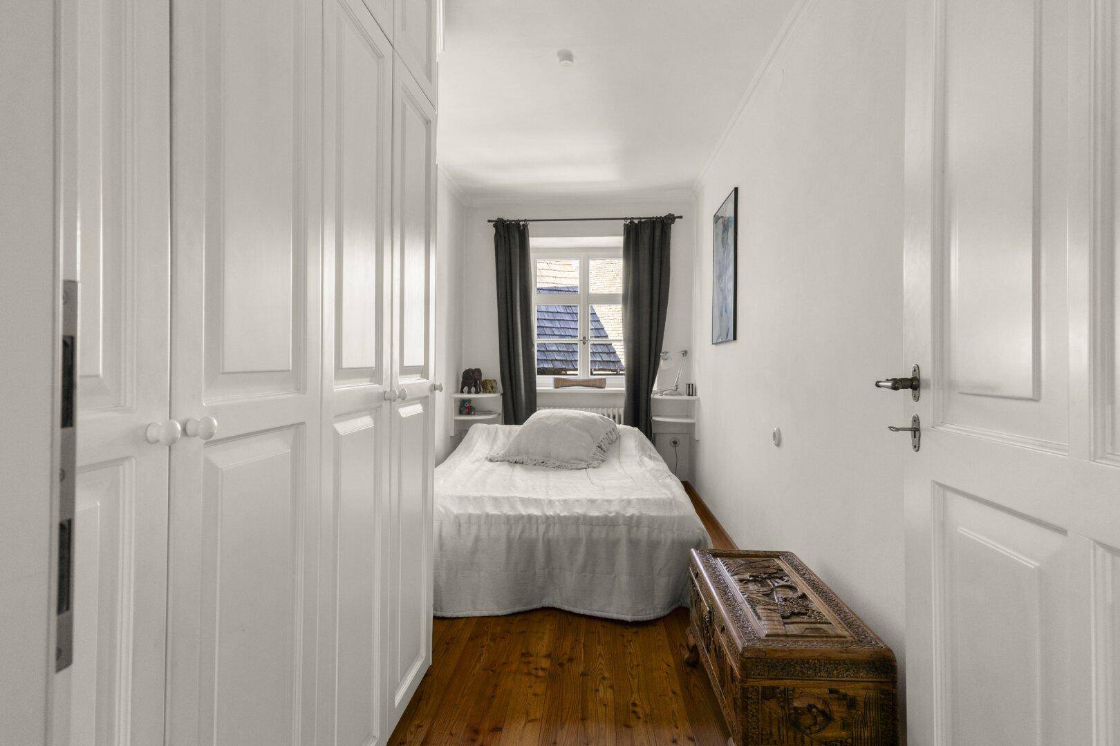 Helles Schlafzimmer mit Holzdielenboden und integrierten weißen Kleiderschränken.