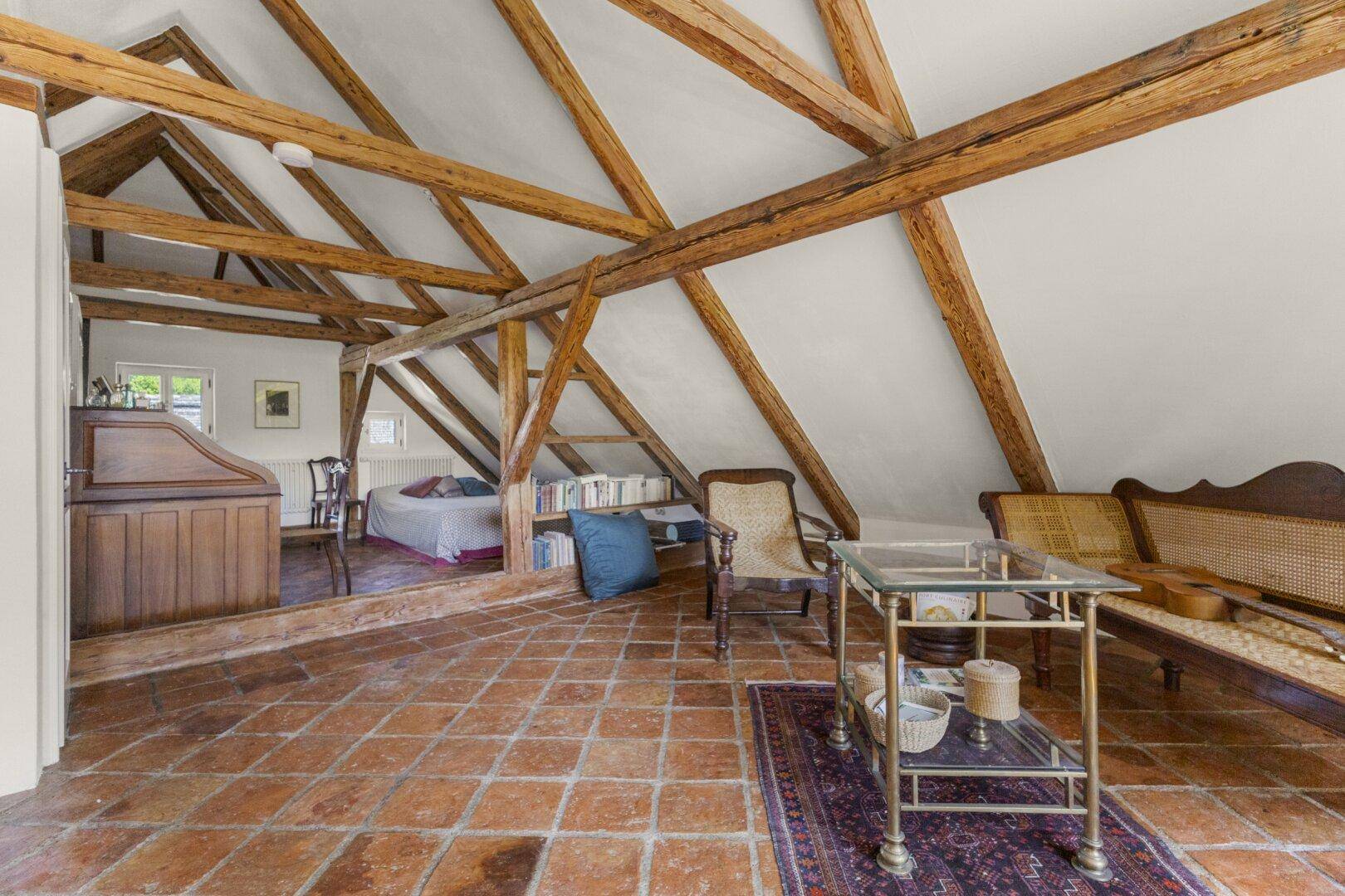 Ausgebauter Dachboden mit sichtbaren Holzbalken, Terrakottaboden und gemütlicher Einrichtung.