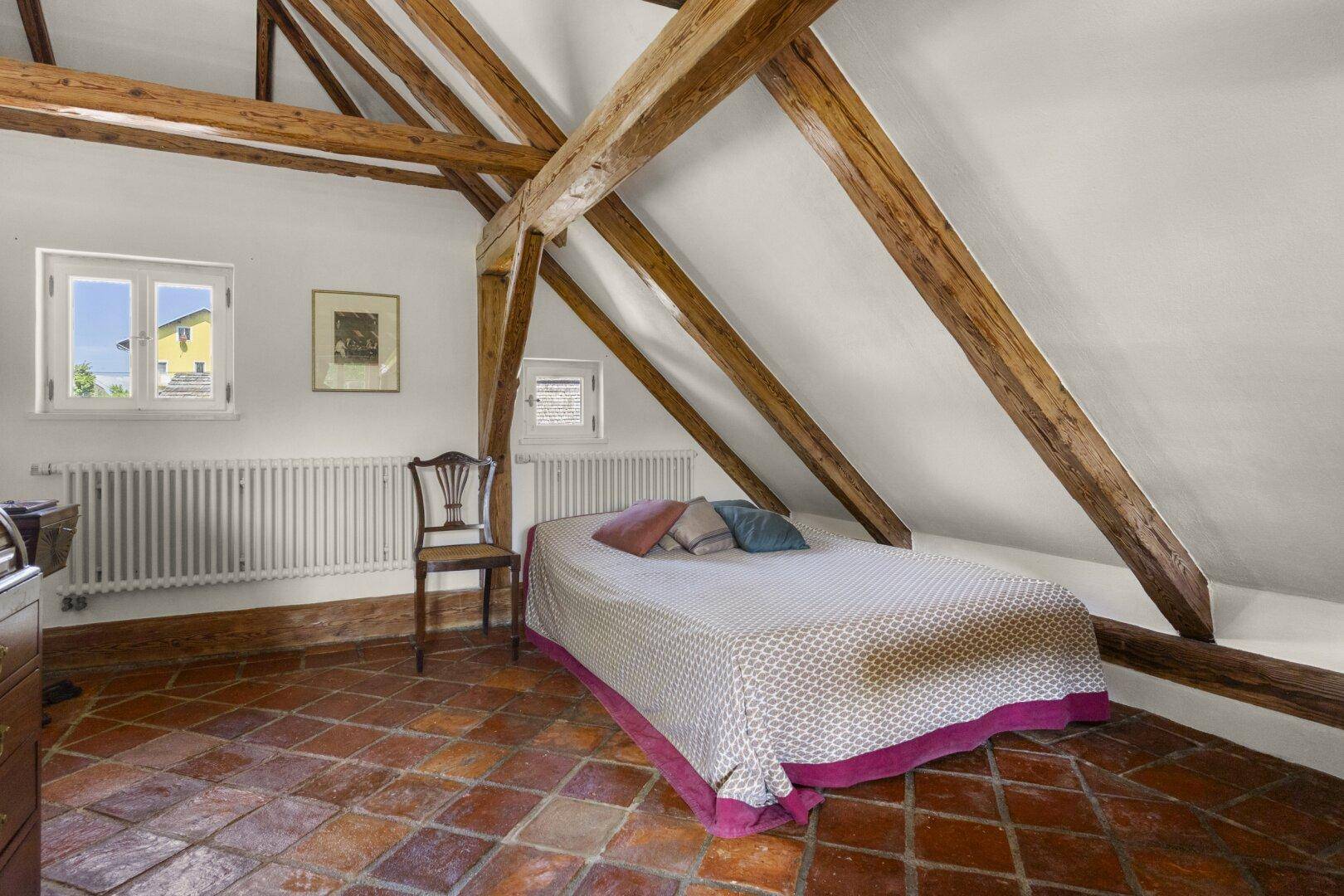 Schlafzimmer im Dachgeschoss mit sichtbaren Holzbalken, Terrakottaboden und schrägen Wänden.