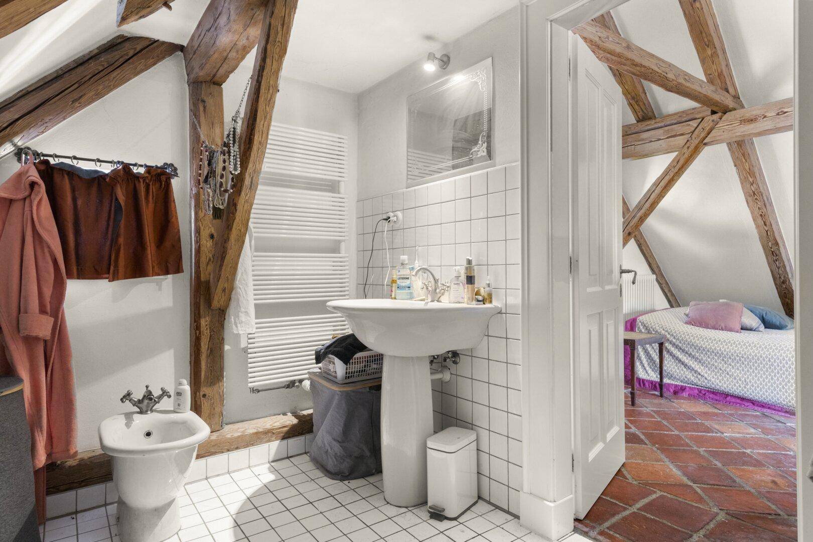 Badezimmer im Dachgeschoss mit weißen Fliesen, Bidet, Waschbecken und beheiztem Handtuchhalter.