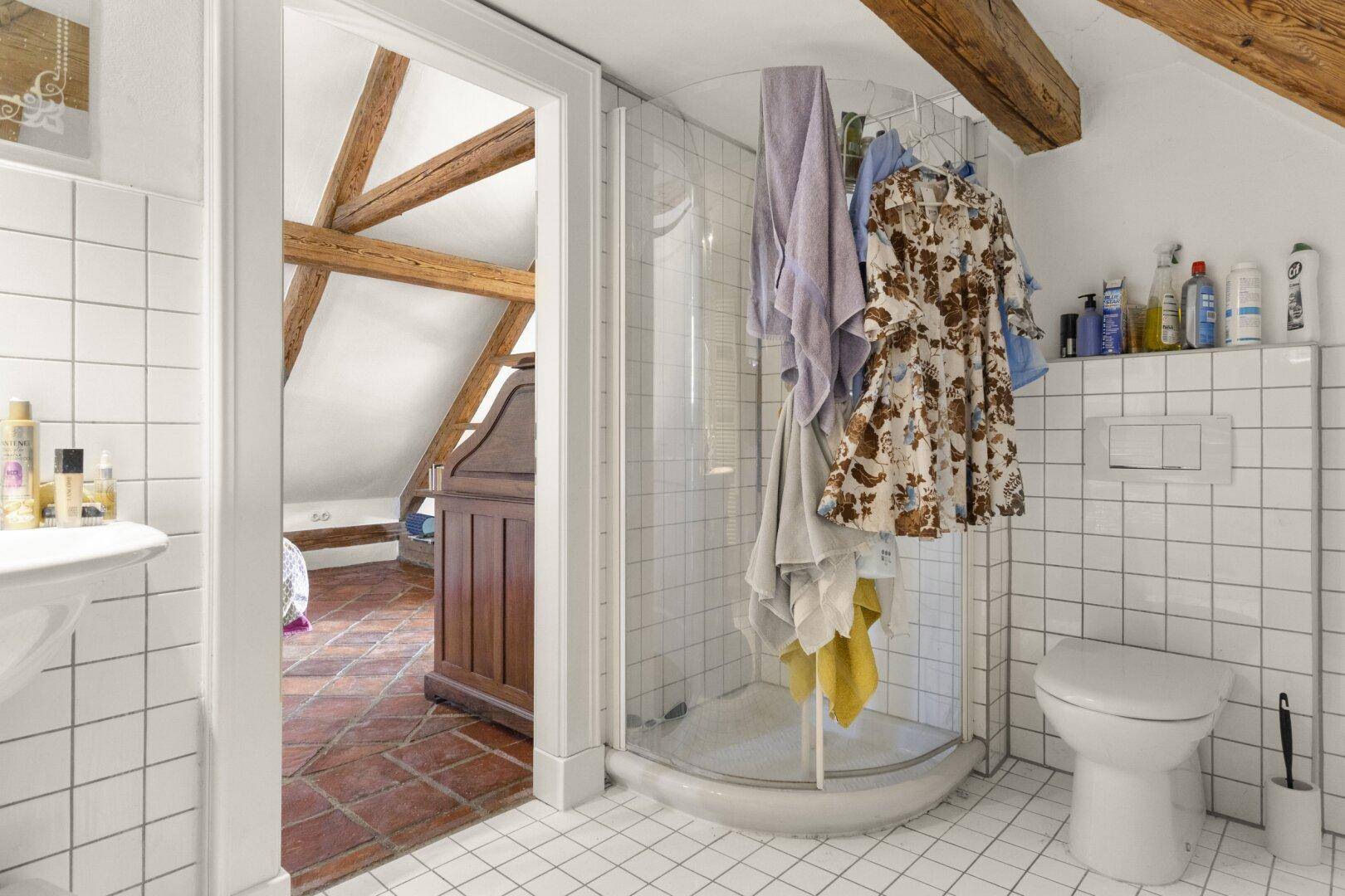Helles Badezimmer im Dachgeschoss mit Duschkabine, Toilette und weißen Fliesen.
