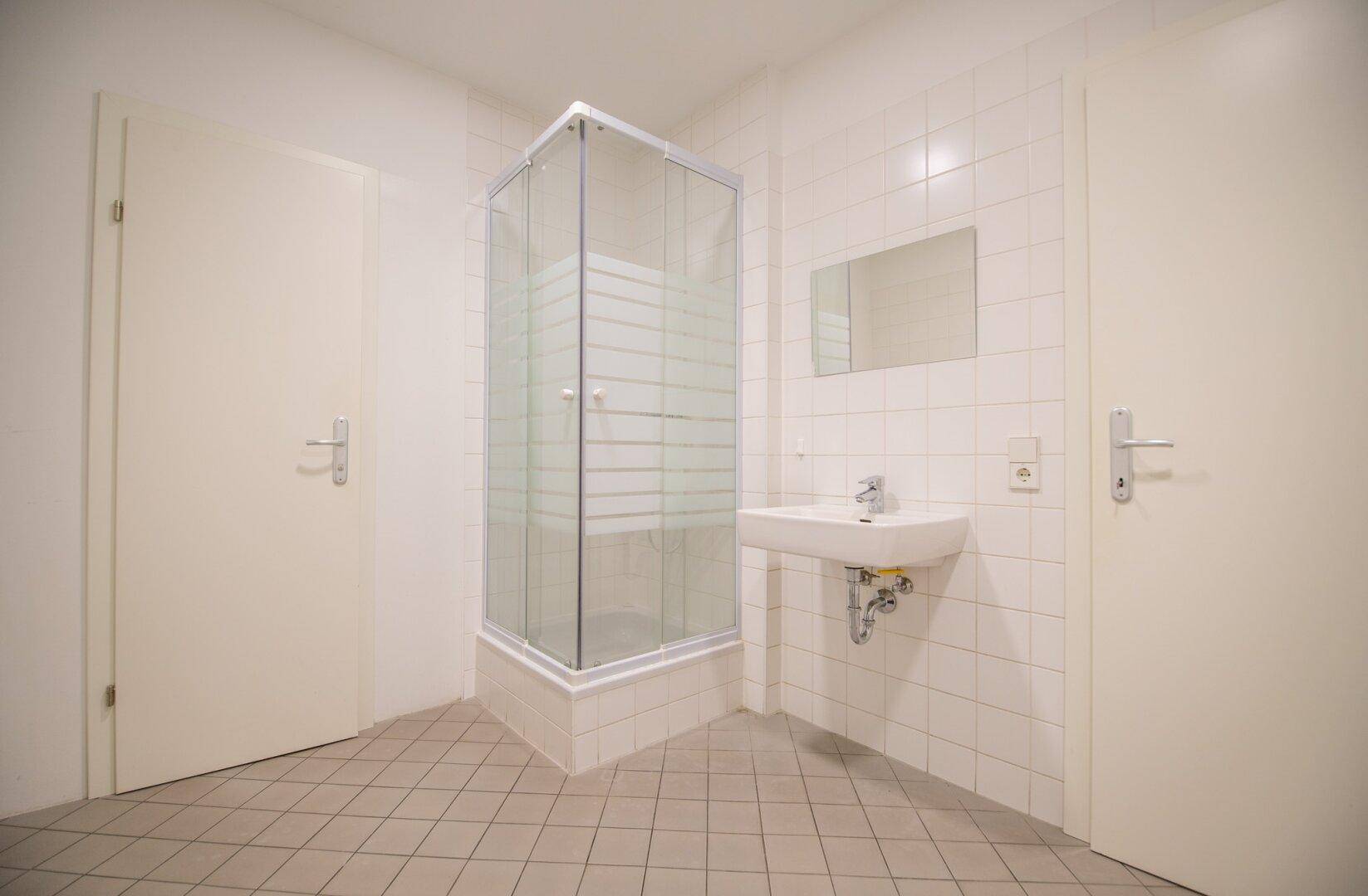 Badezimmer mit Duschkabine, Waschbecken und hellen Fliesen an Wänden und Boden.