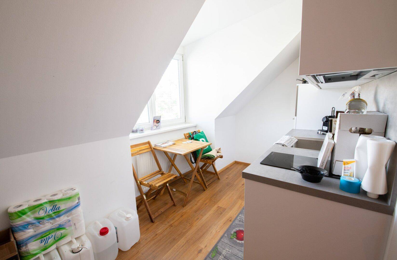 Kleine Küchenzeile unter einer Dachschräge mit Esstisch, Fenster und Induktionskochfeld, funktional eingerichtet.