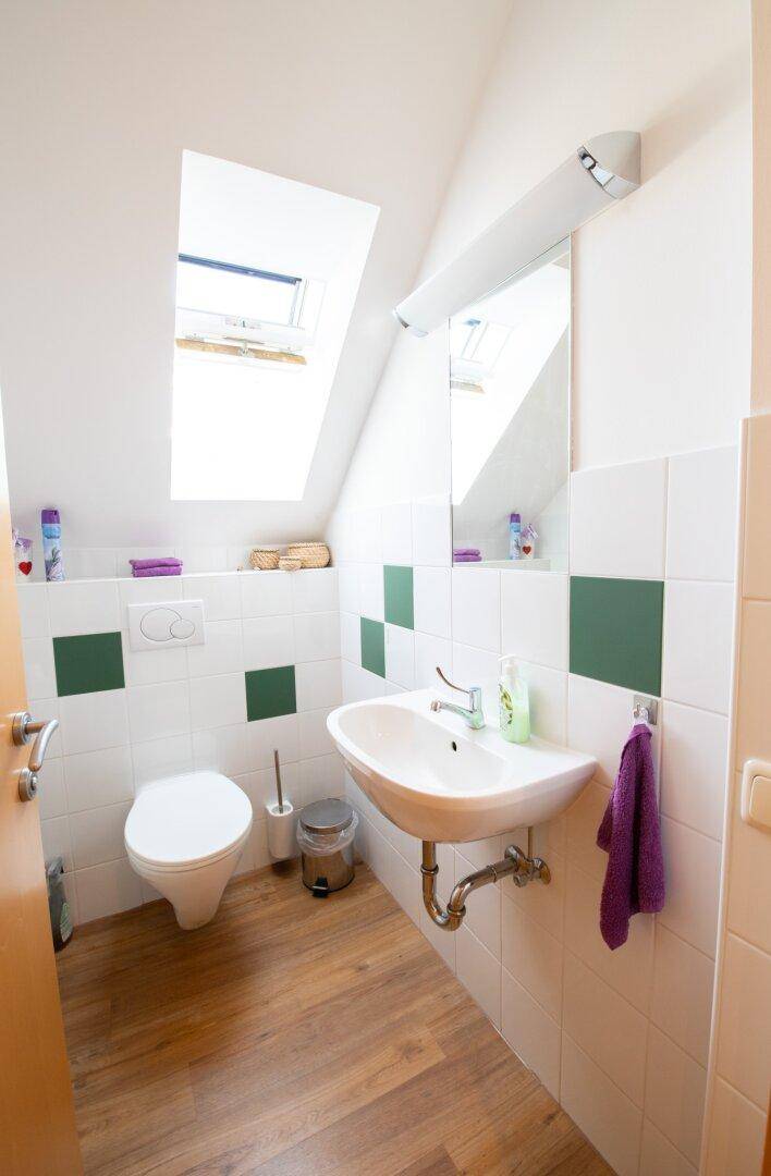 Badezimmer mit Dachschräge, Dachfenster, WC und Waschbecken, gefliest in Weiß und Grün, sehr gepflegt.