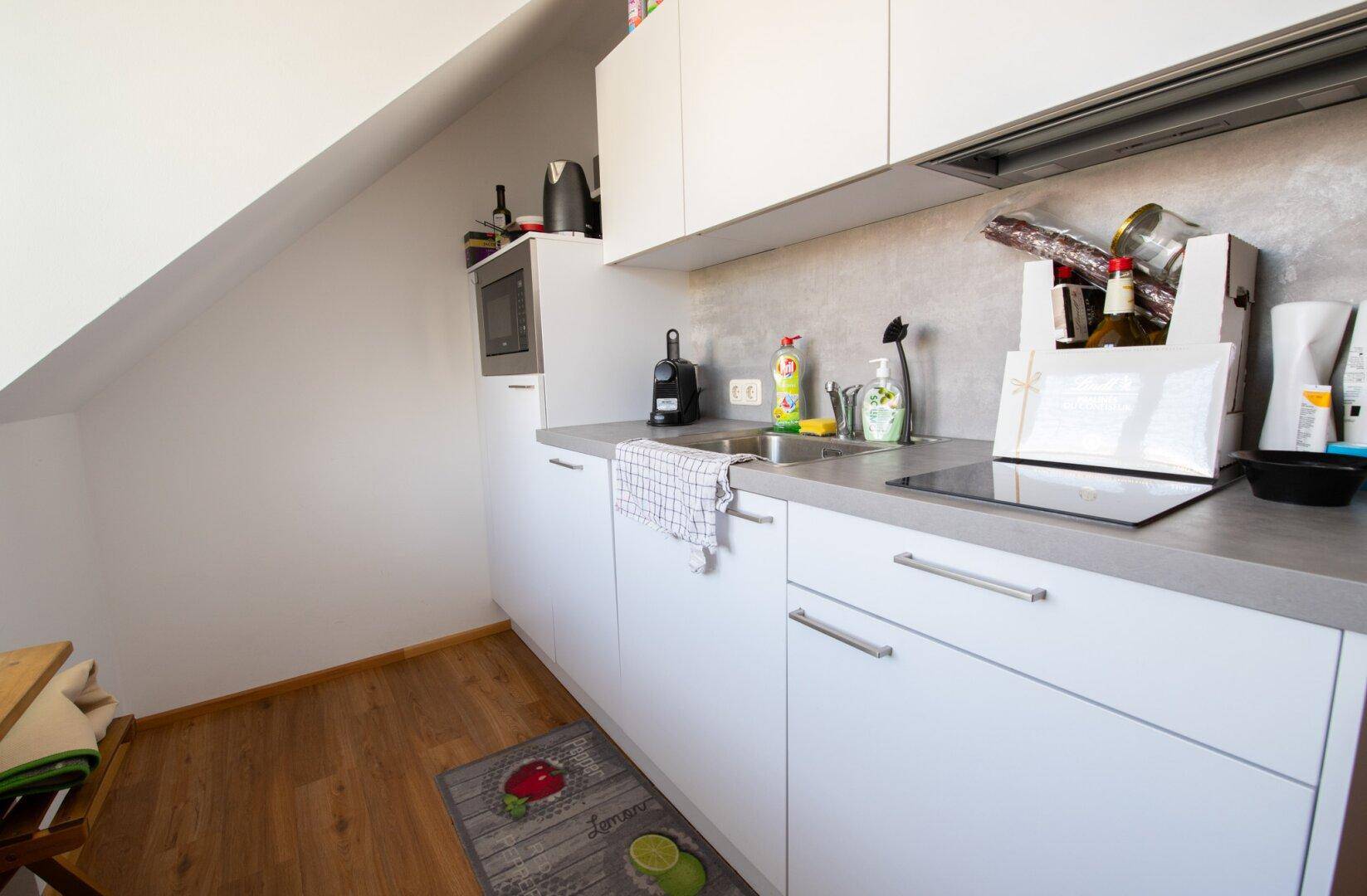 Moderne Küchenzeile mit weißen Schränken, Spüle und Induktionskochfeld unter einer Dachschräge, gut ausgestattet.